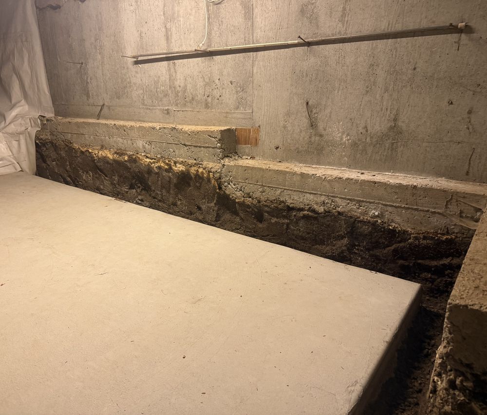 Basement with the existing footing exposed along a concrete wall before repair.