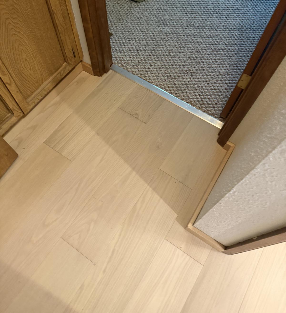 Light wood-tone plank flooring meeting carpet at a doorway in a Portland-area home